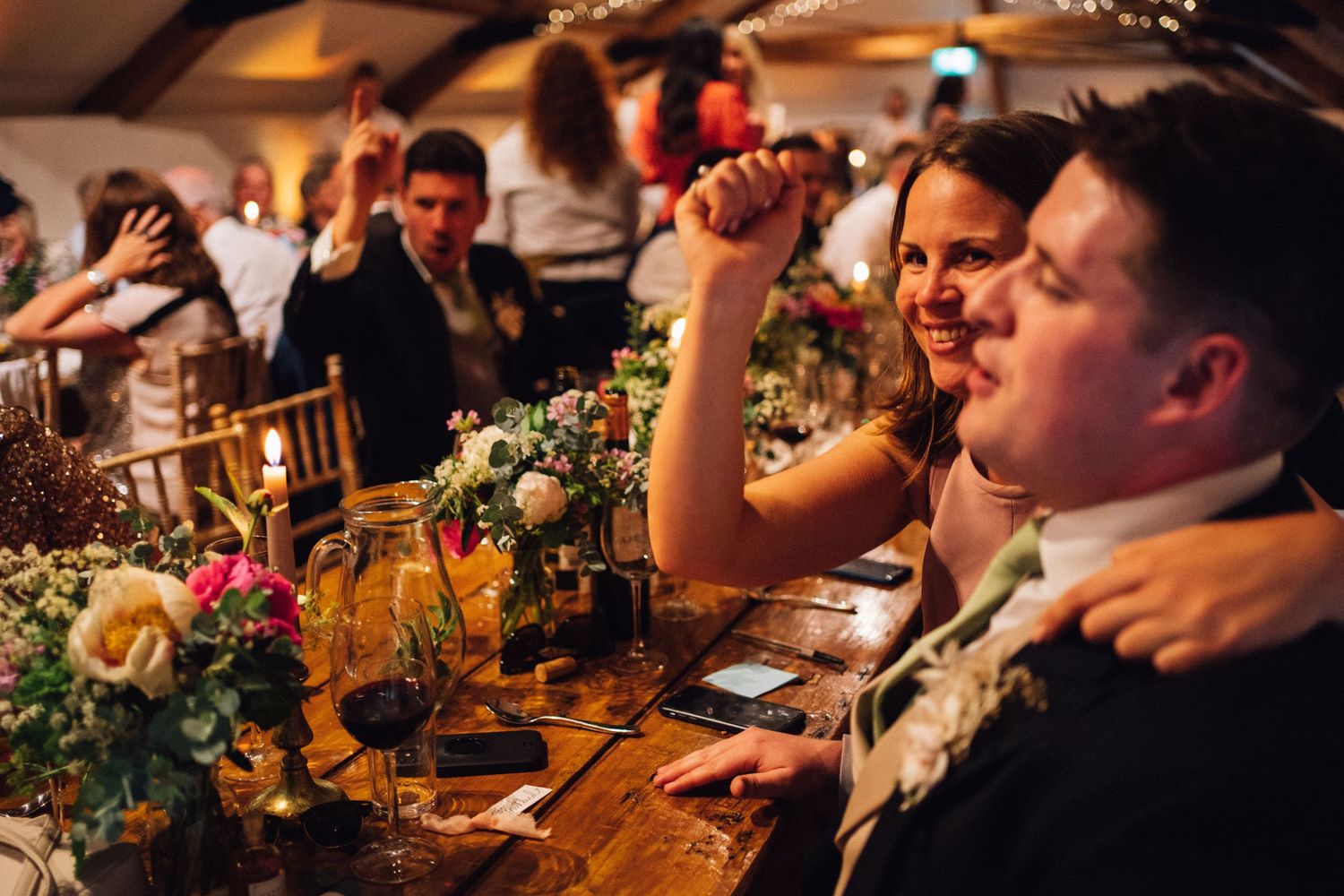 Wedding reception celebration with festive lighting and floral centerpieces at a wooden table.