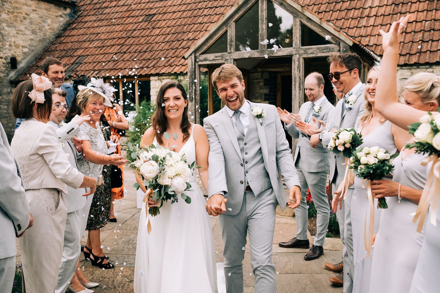 Wedding party celebrates on a rustic outdoor patio with brick walls and terracotta roof tiles.