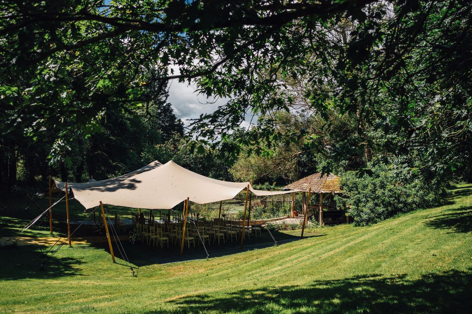 White tent canopies set up on a lush green lawn surrounded by trees for an outdoor event.