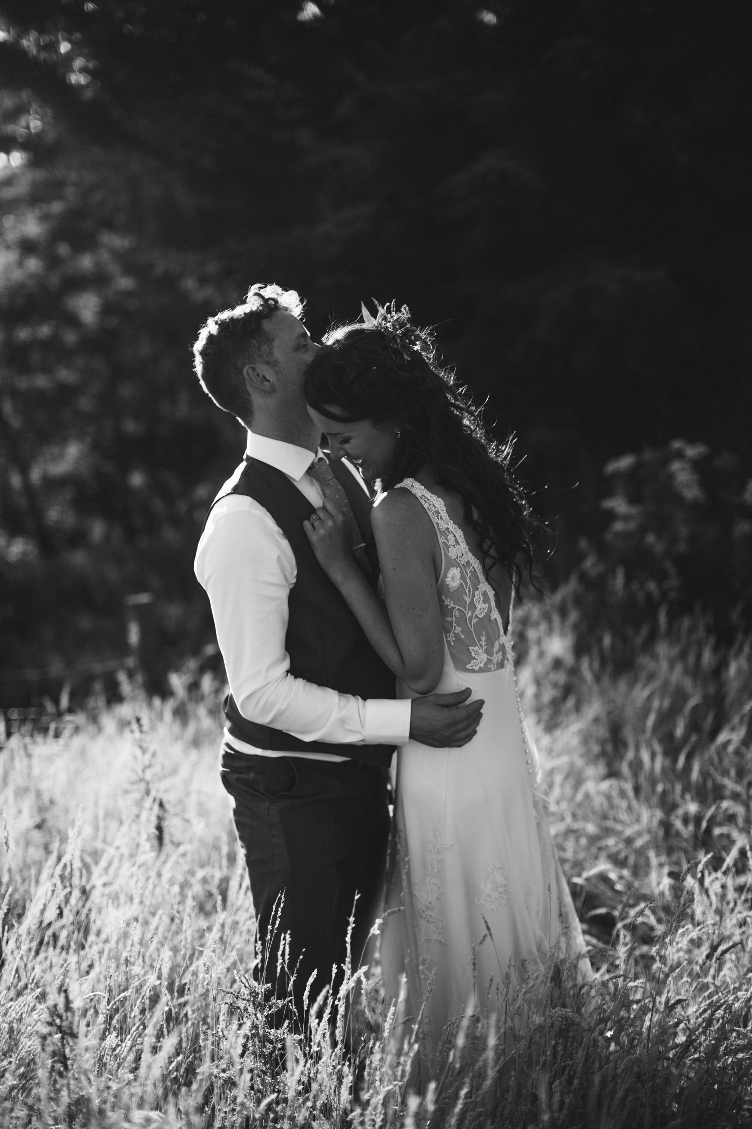 Black and white wedding portrait showing tender moment in tall grass field.