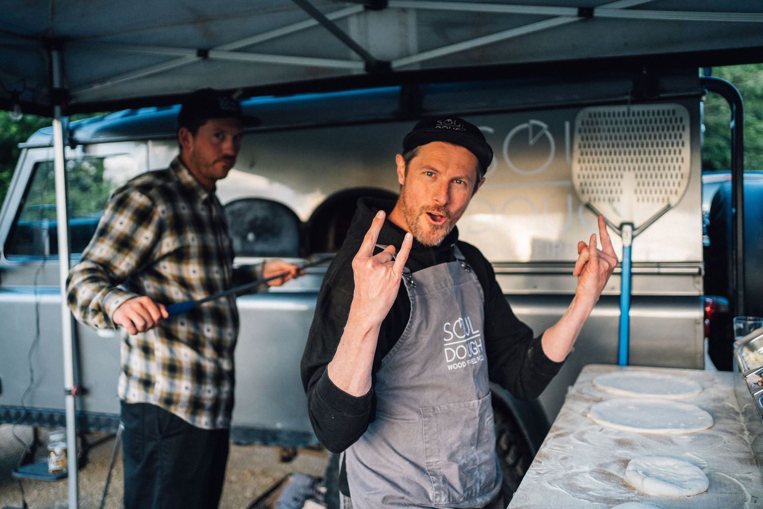 Food truck vendors preparing meals under a white canopy tent at an outdoor event.