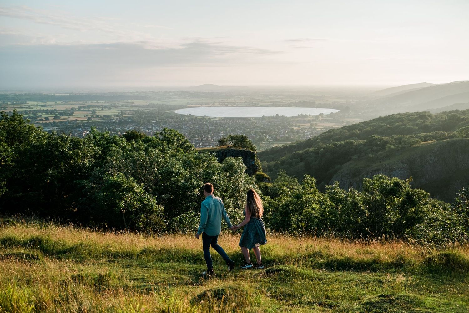 Sweeping landscape vista of hills and water with people enjoying the scenic overlook.