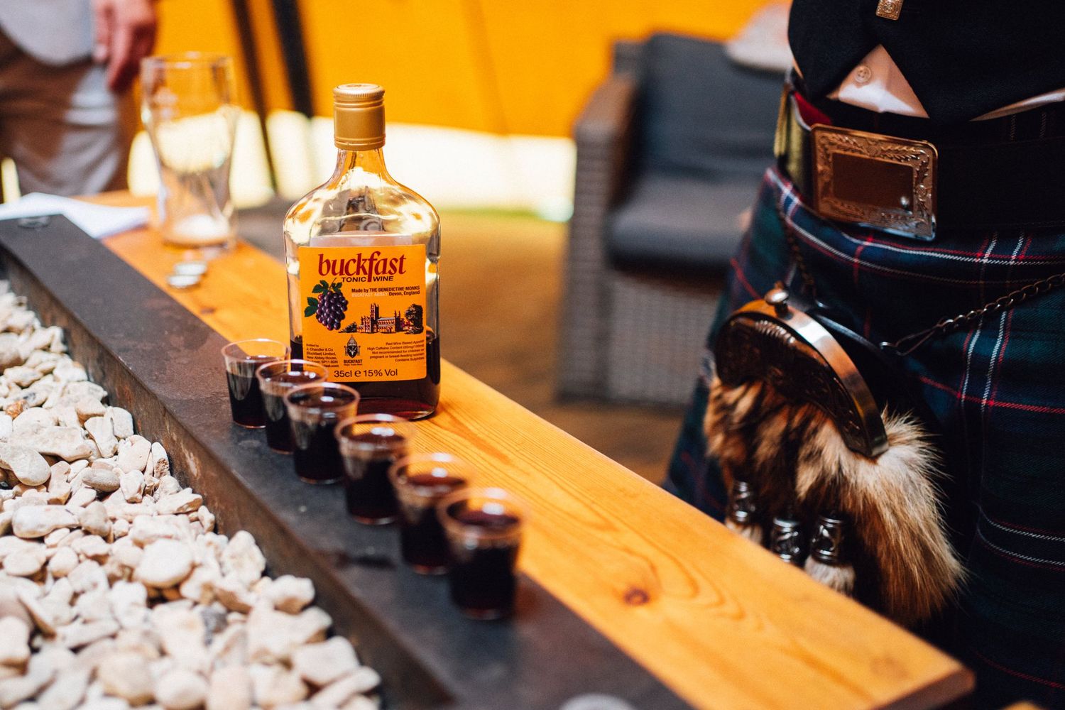 Bottle of whiskey with shot glasses lined up on wooden bar top.