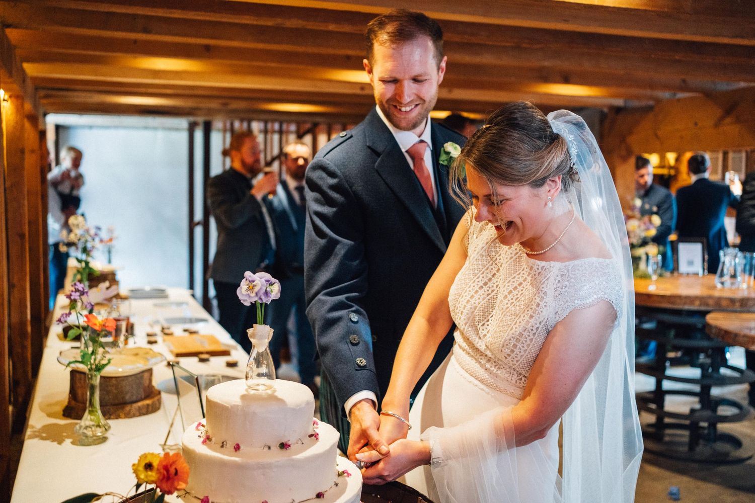 Couple cuts their white tiered wedding cake together during reception.
