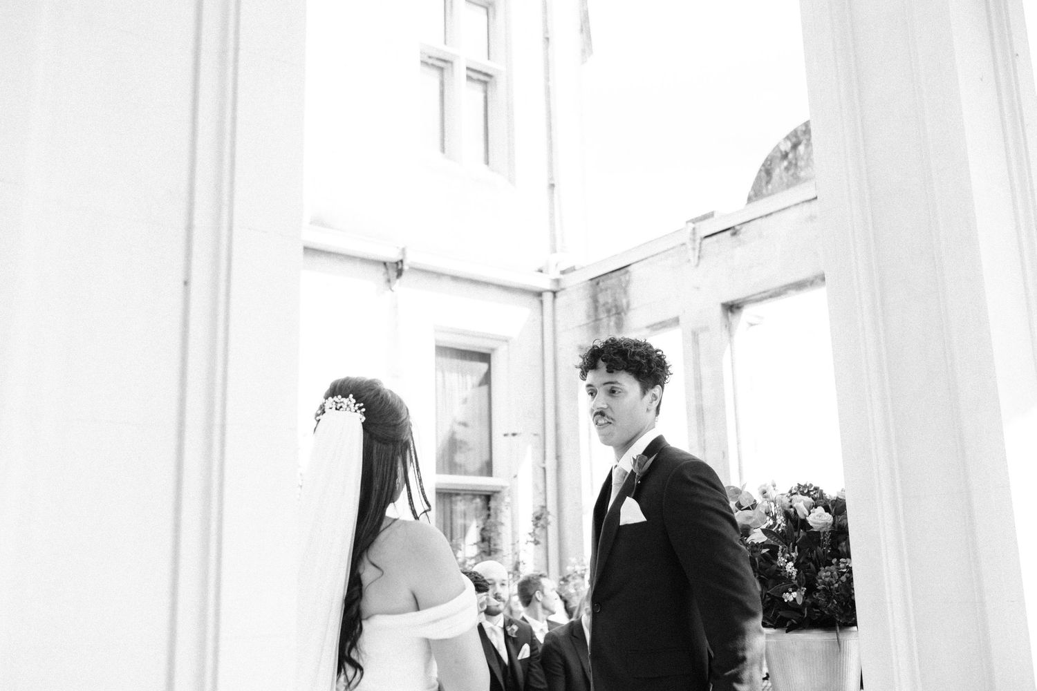 A black and white wedding photo showing a couple exchanging vows in an elegant venue.