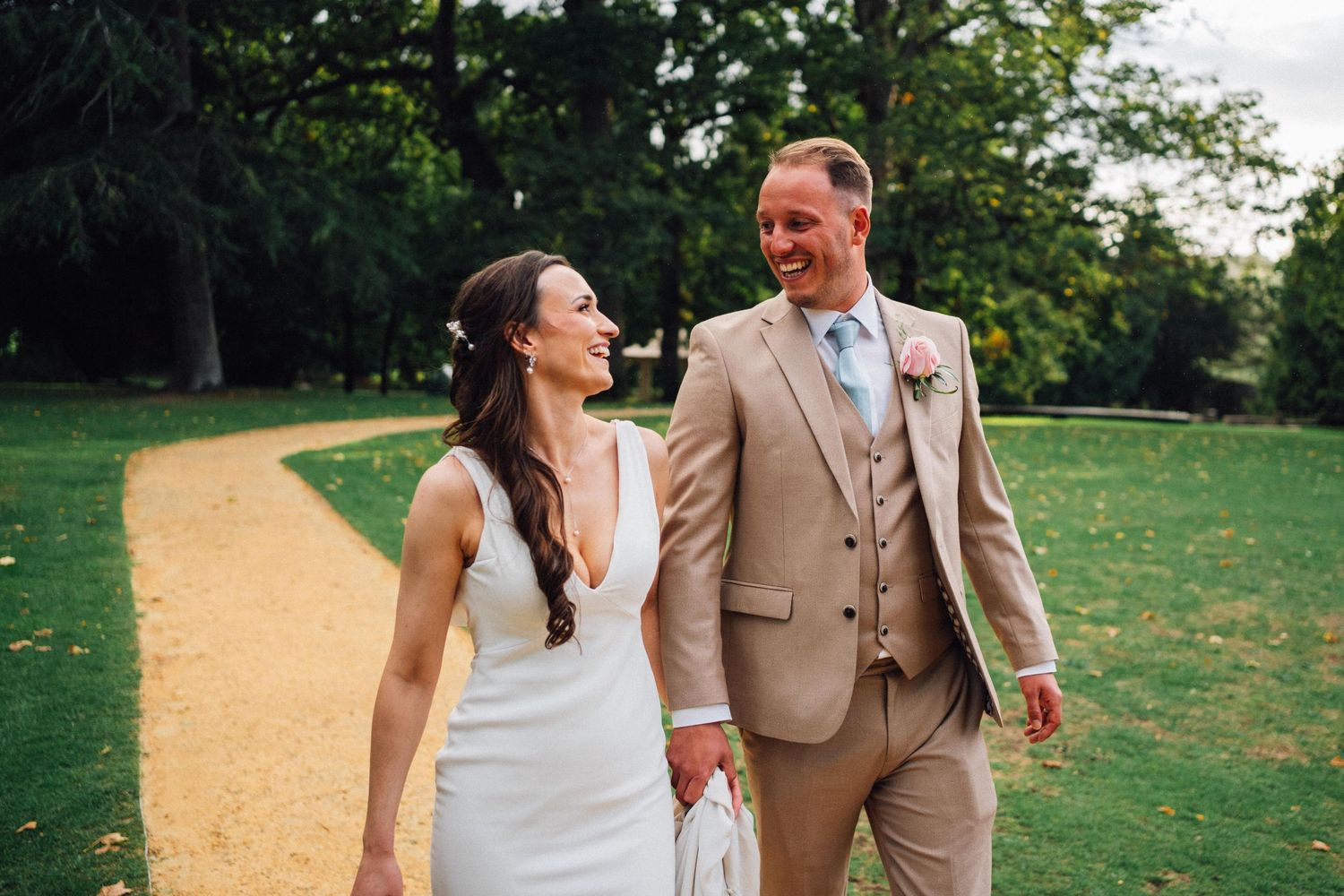 Newlyweds walking together on garden path during summer wedding photoshoot.