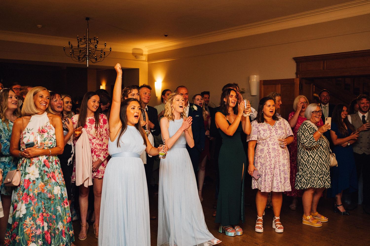 Wedding guests in colorful dresses celebrate enthusiastically during the evening reception.