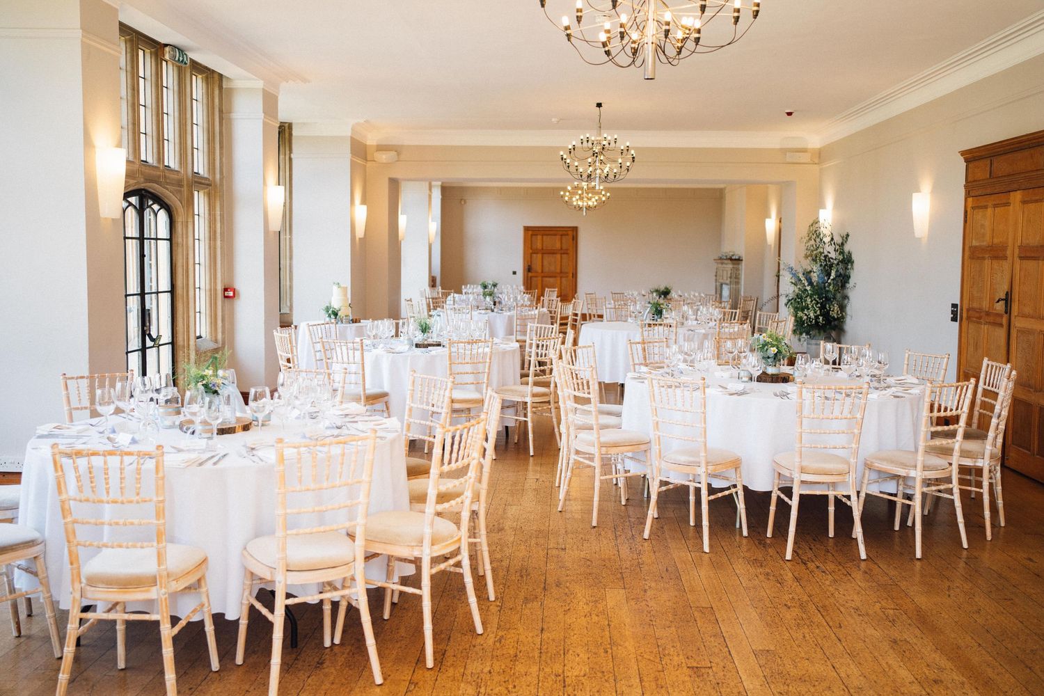 Elegant wedding reception venue with white chairs and tables arranged under crystal chandeliers in a bright banquet hall.