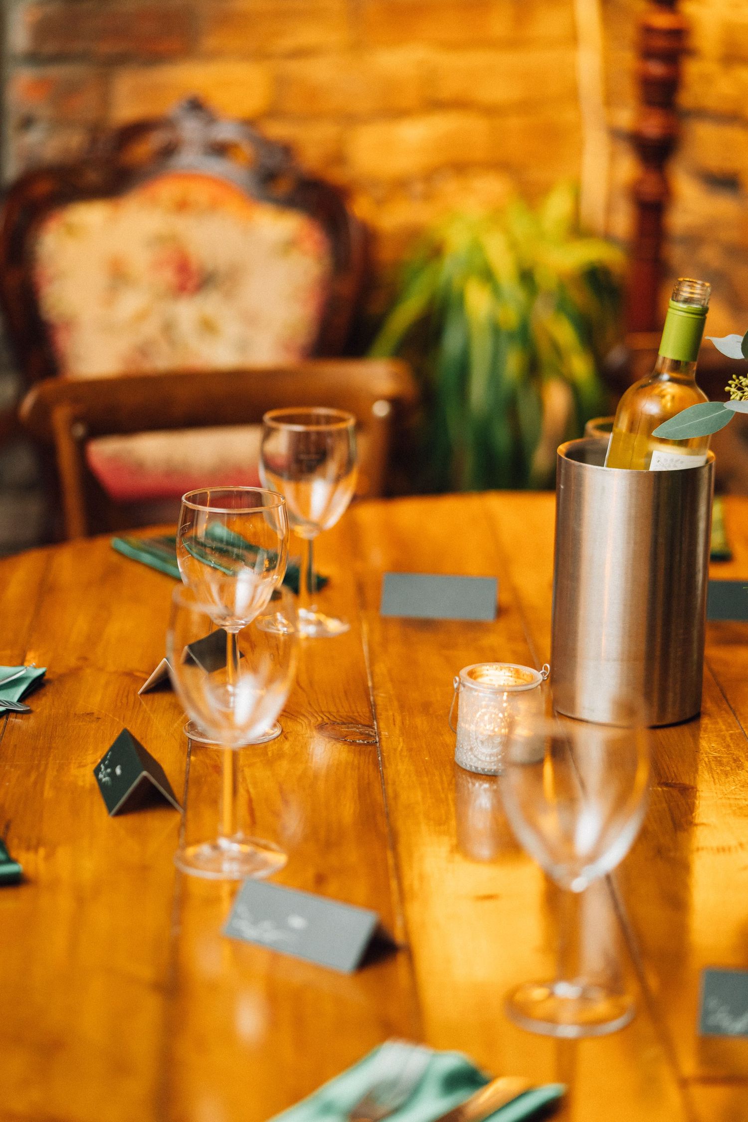 Wine glasses and place settings arranged on a wooden table with turquoise name cards and ambient lighting.