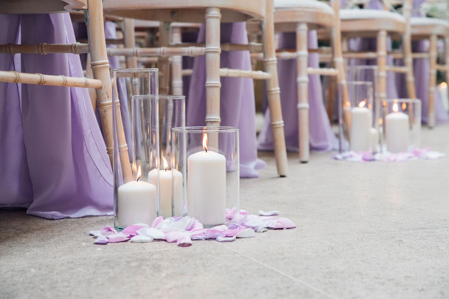 Wedding ceremony setup with rows of chairs draped in soft purple fabric and white floral decorations.