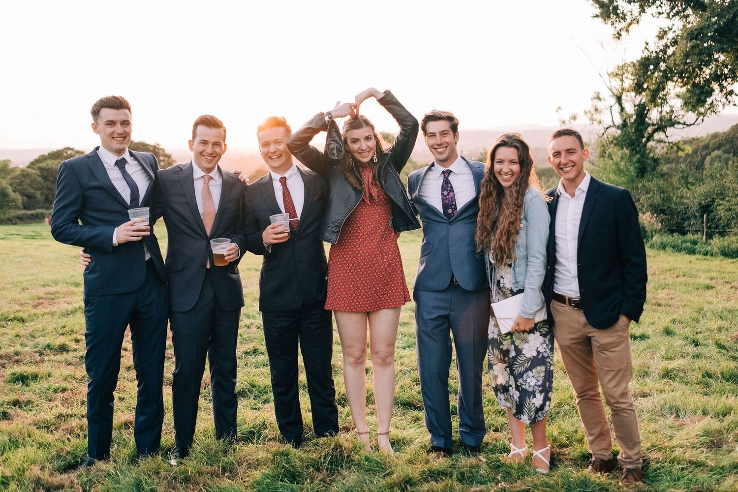 Large wedding party group poses outdoors in casual formation wearing mix of formal attire.