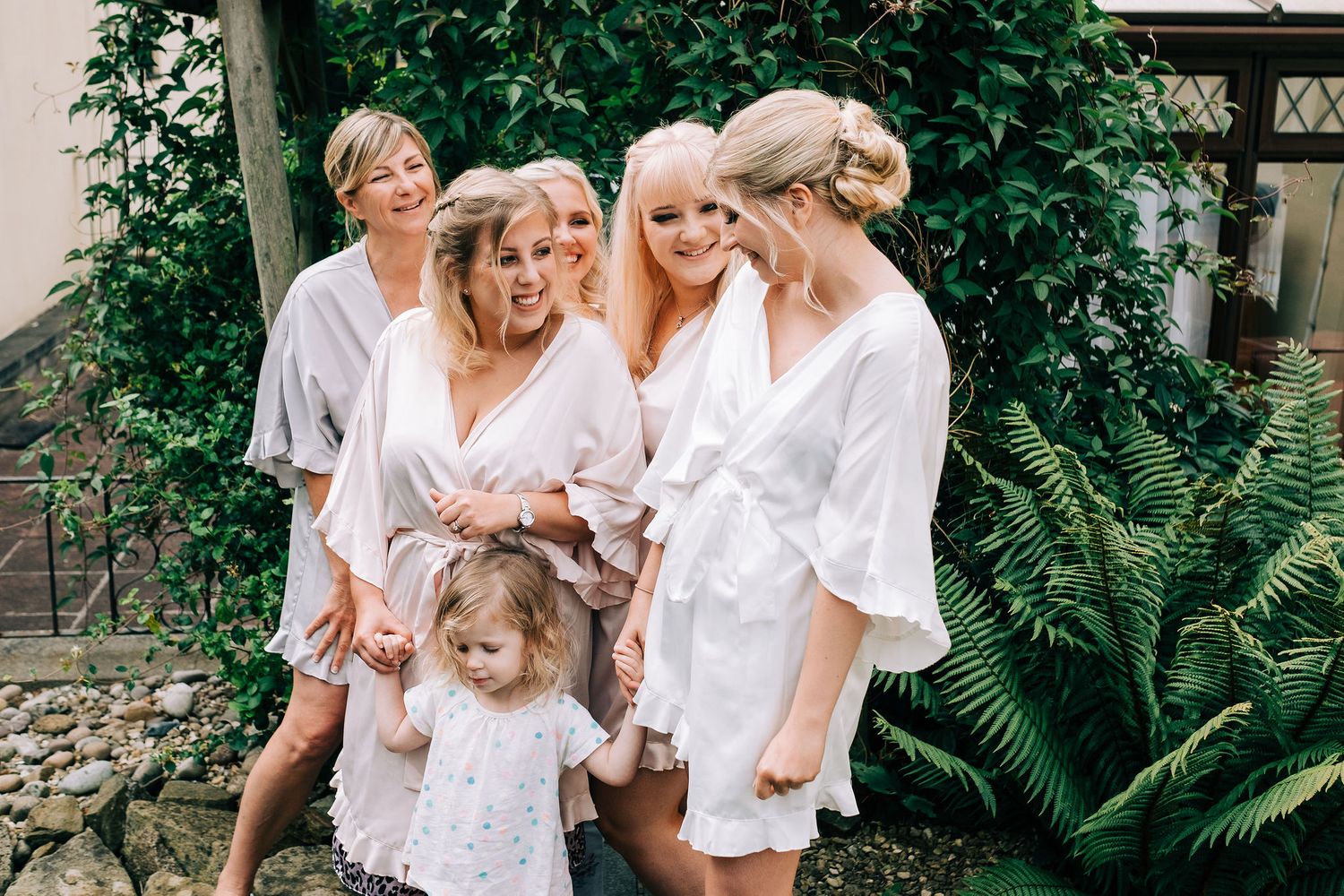 People in white outfits gathered outdoors among tropical plants and greenery.