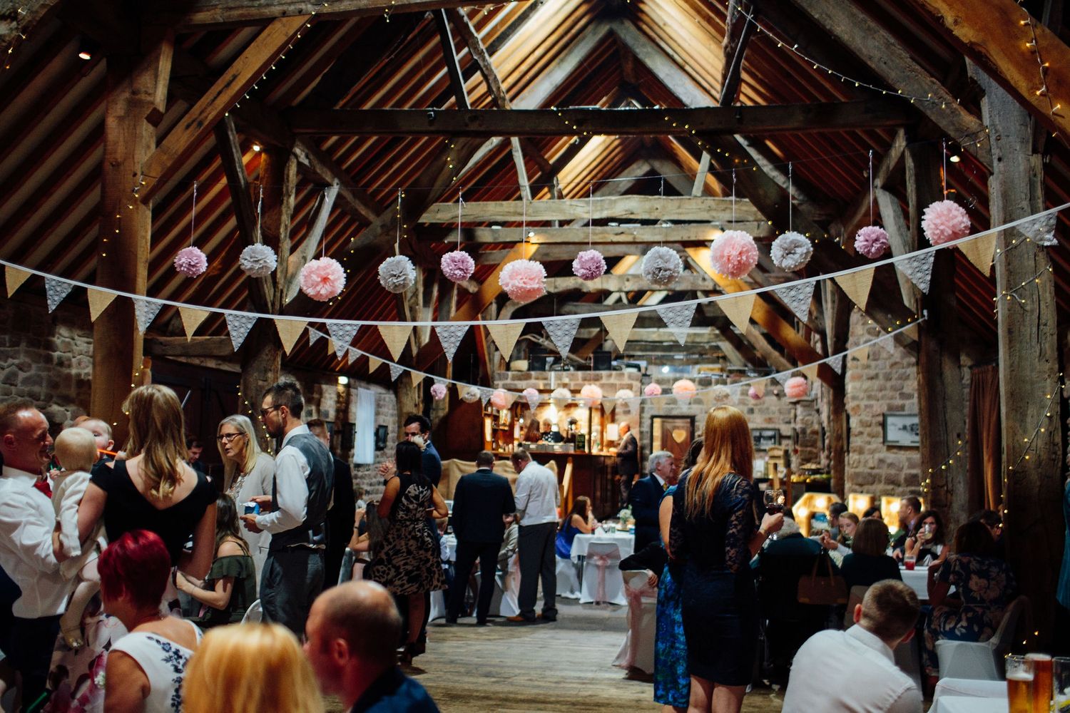 Wedding celebration in a rustic barn venue with hanging bunting decorations and festive lighting.