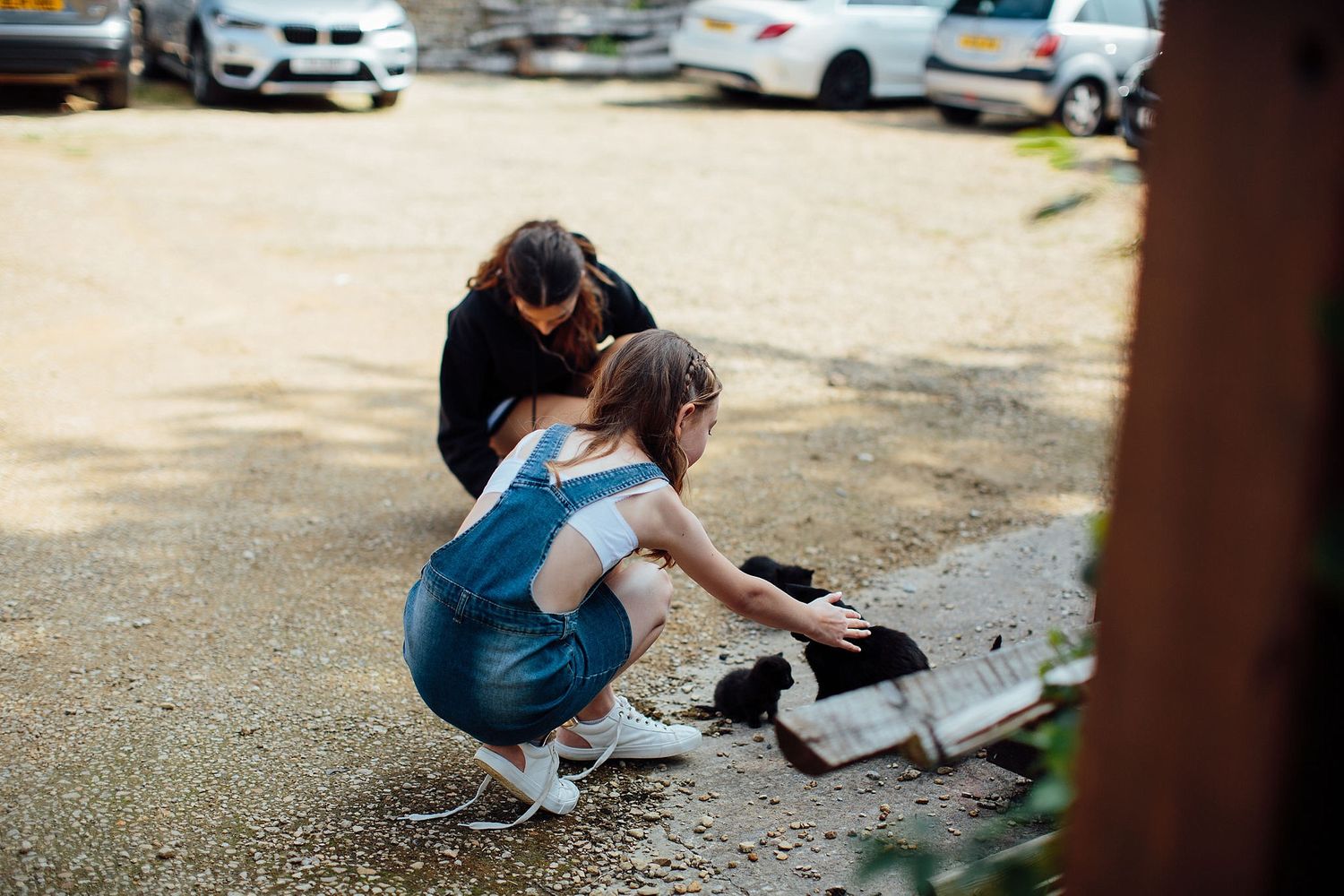Two people crouch down to pet a cat in a parking lot.