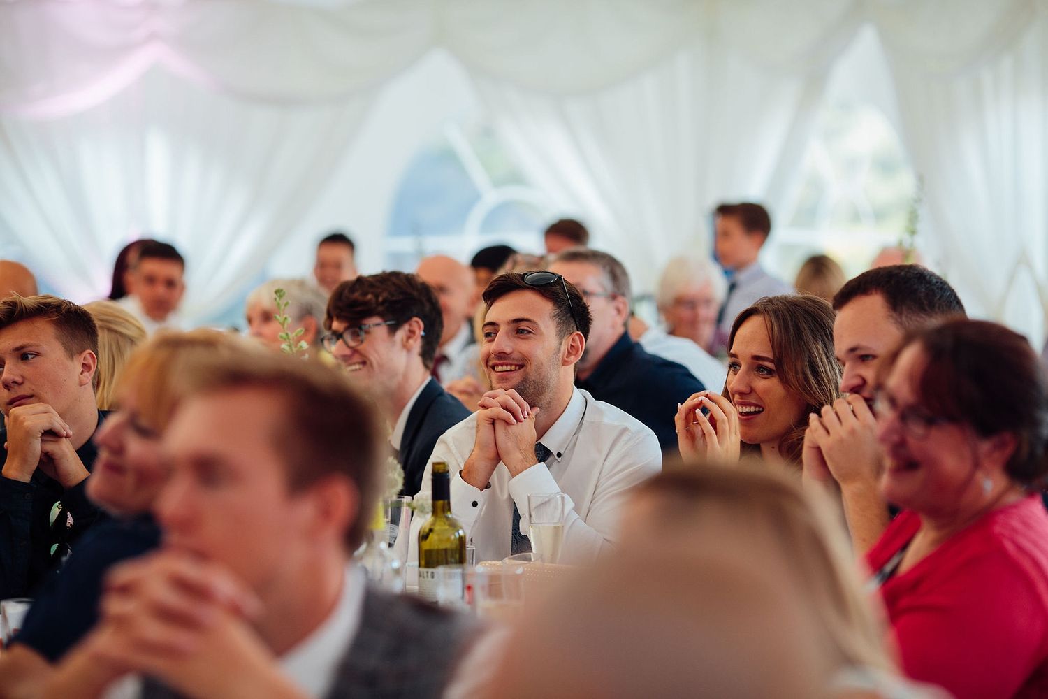 Wedding reception guests seated at tables in a marquee tent.