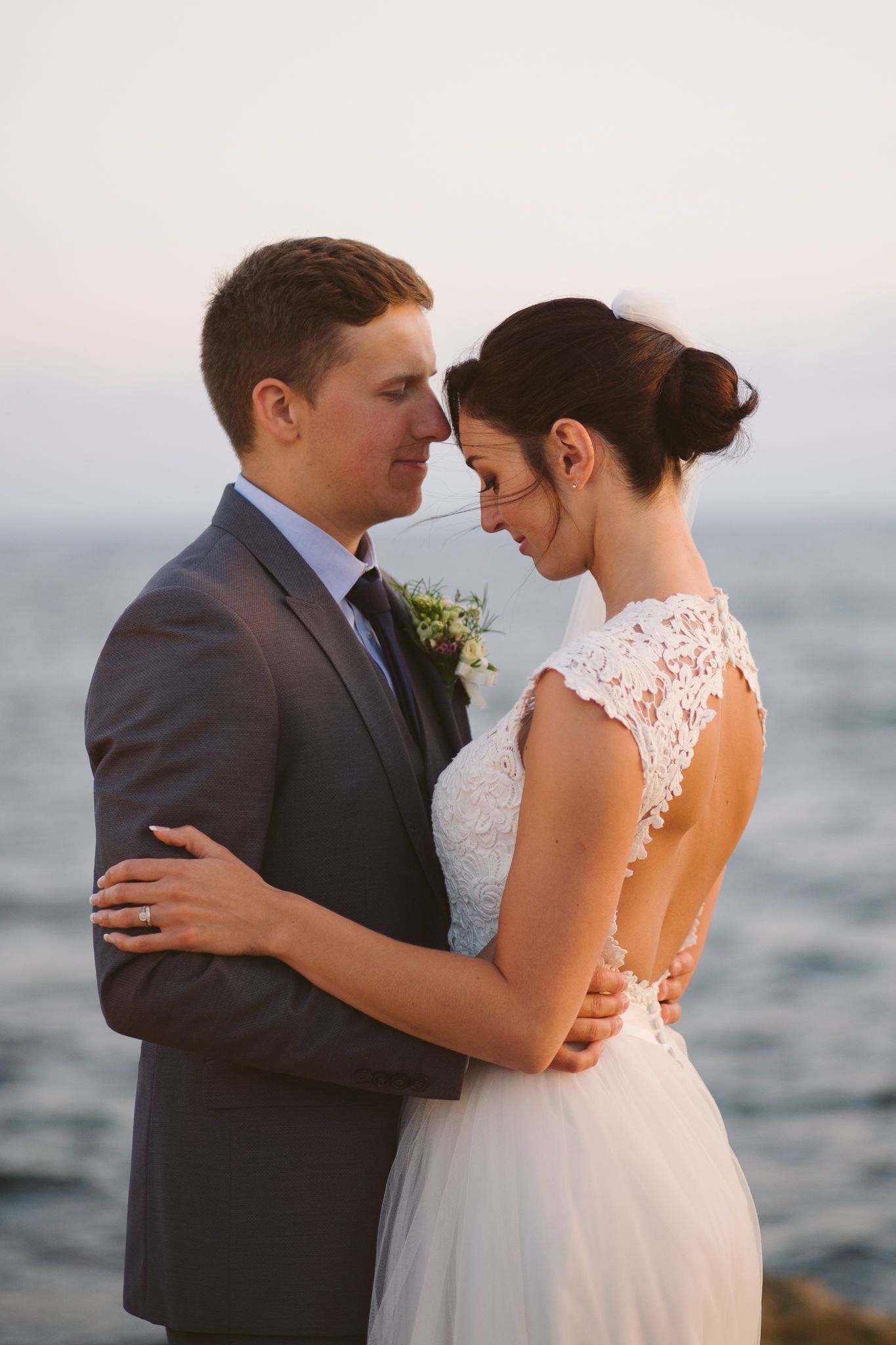 An intimate moment between newlyweds embracing by the ocean at sunset.