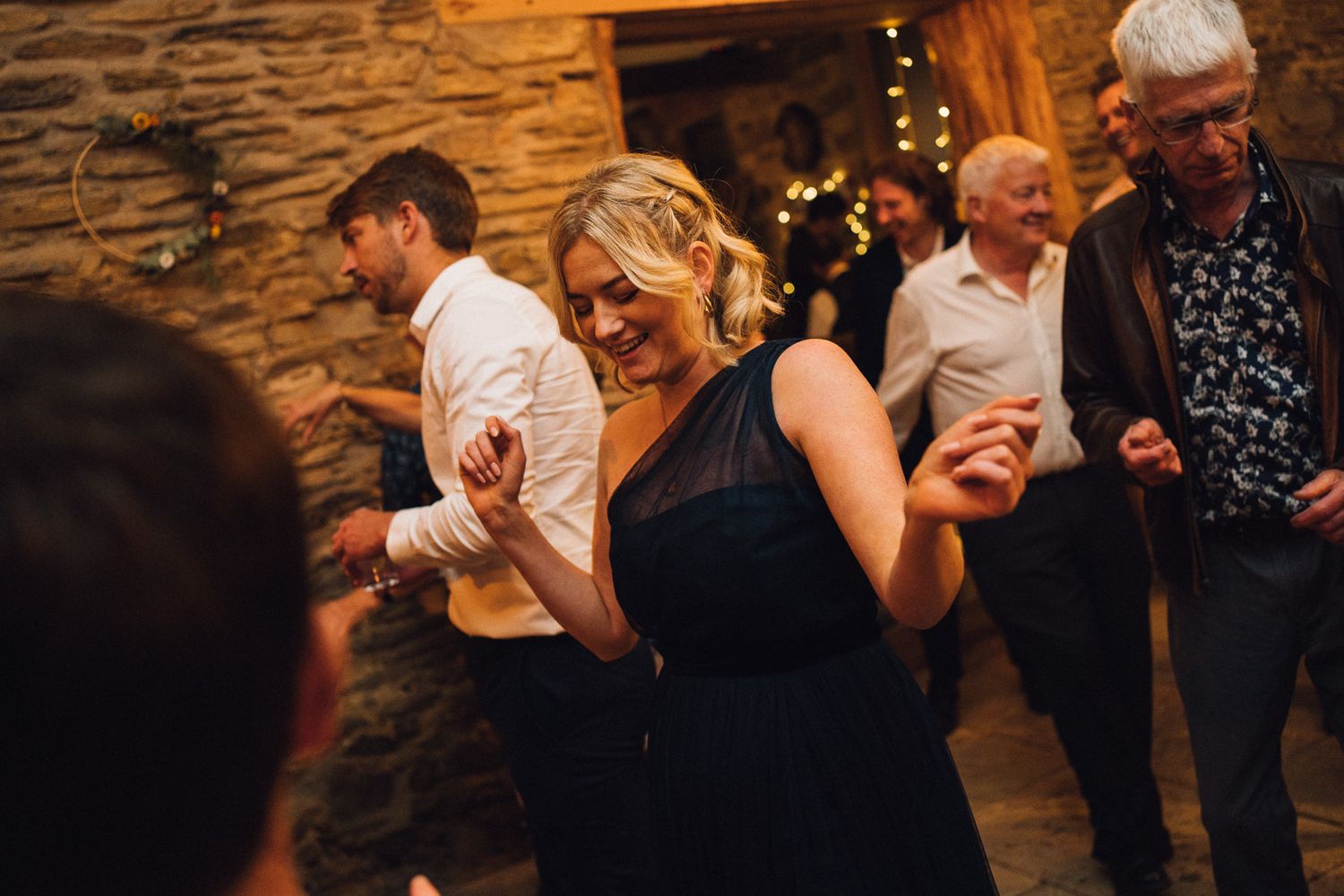 Couples dancing together at wedding reception with warm lighting and stone walls.