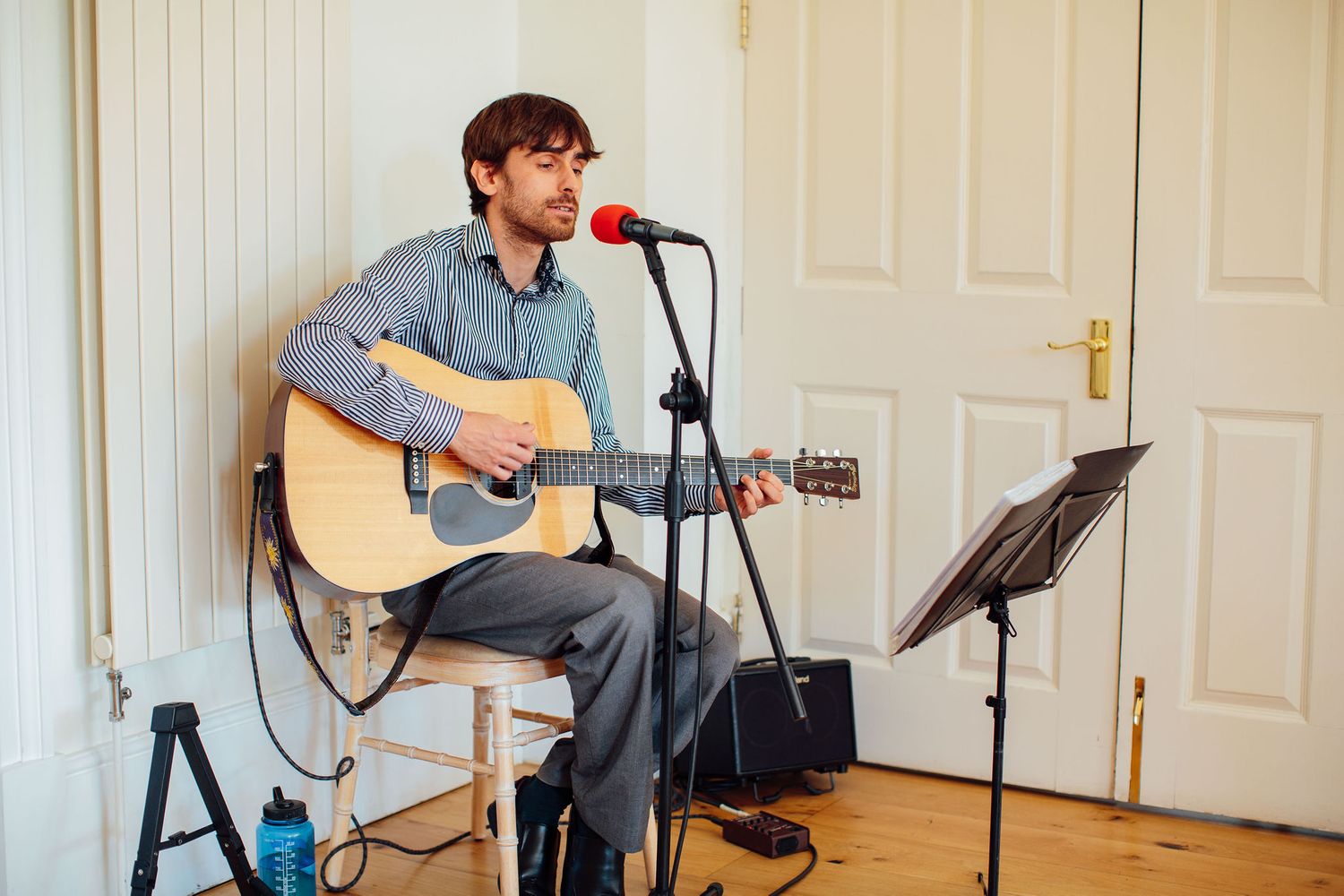 Musicians performing with acoustic guitars and microphones in a bright indoor space.