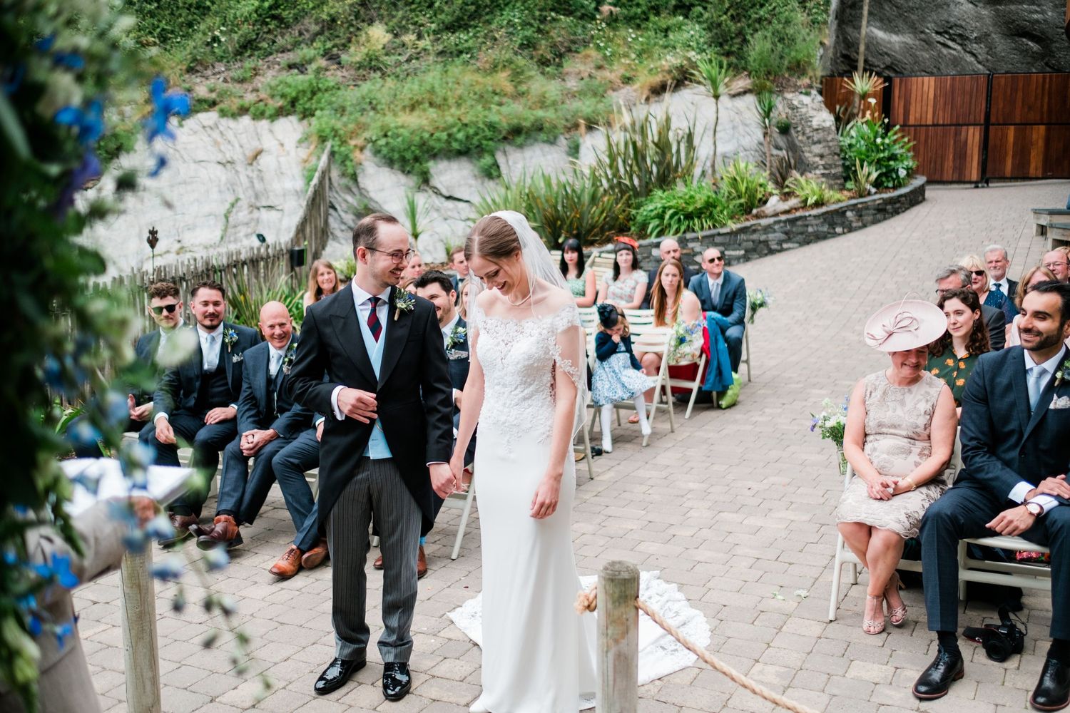 Wedding ceremony procession on stone pathway with guests watching from sides.