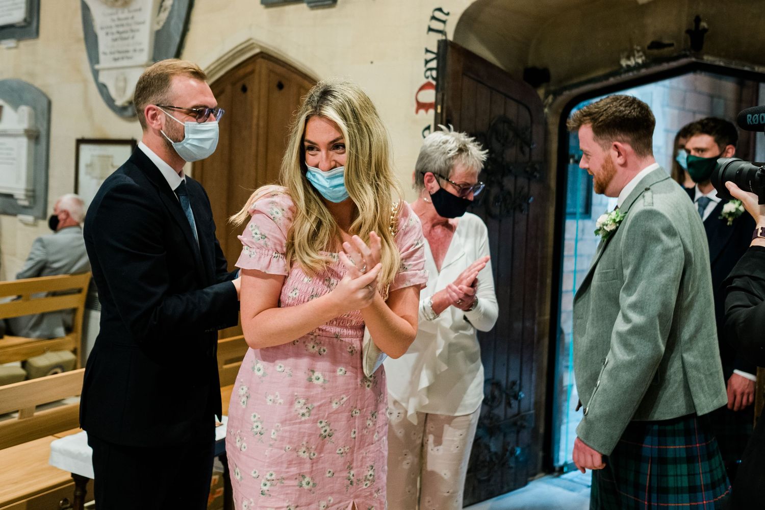 Wedding guests mingling inside church wearing formal attire and protective masks.