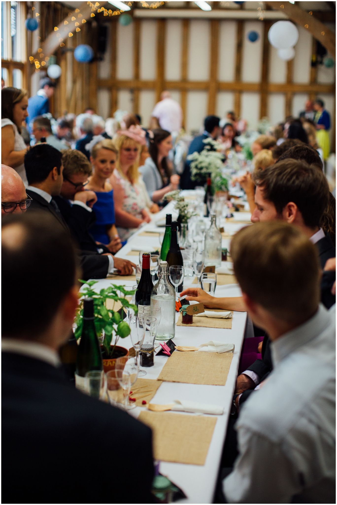 Wedding guests seated at long tables during an indoor barn reception.