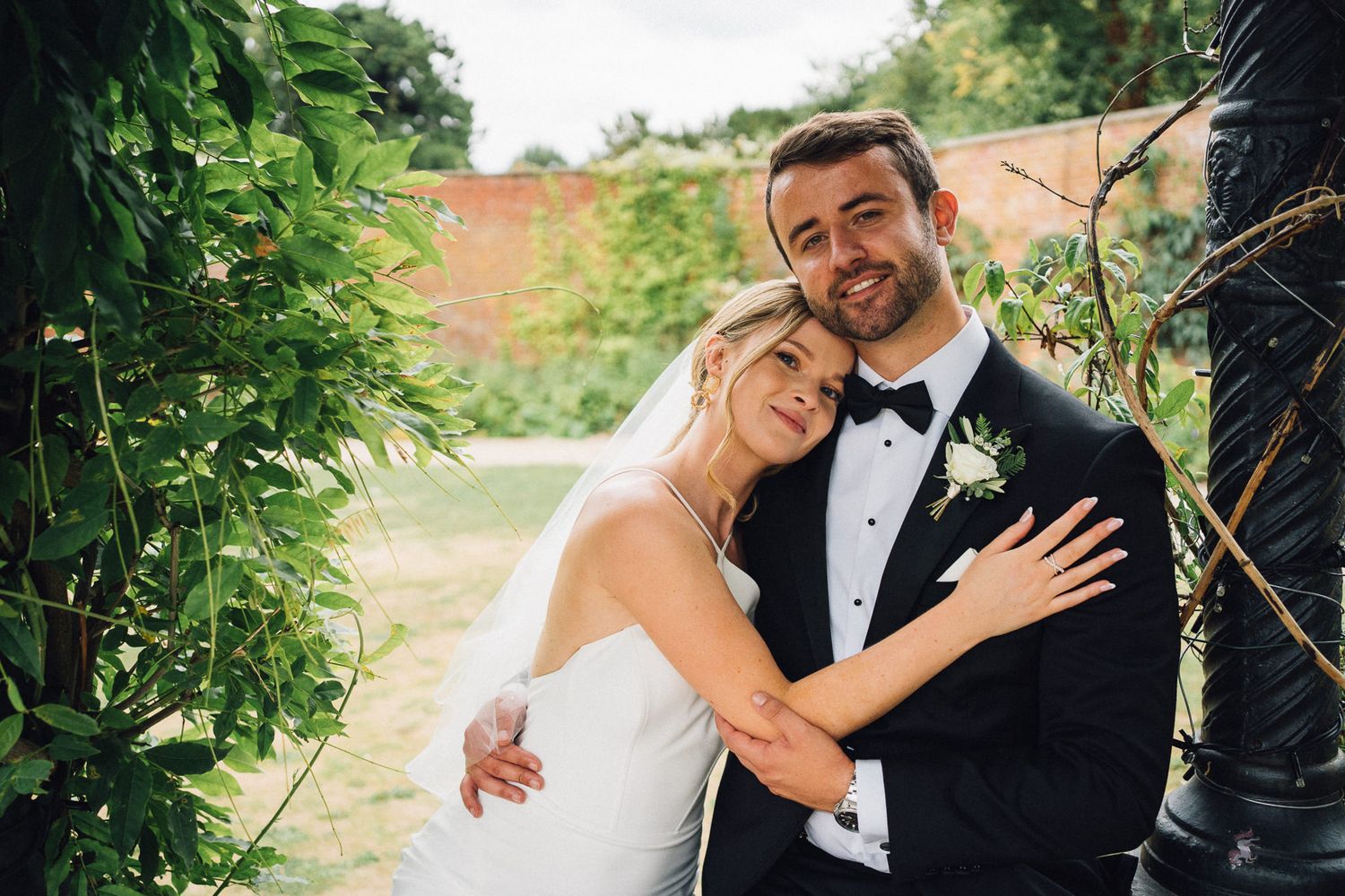 Intimate wedding moment captured in a garden with natural greenery and brick wall.