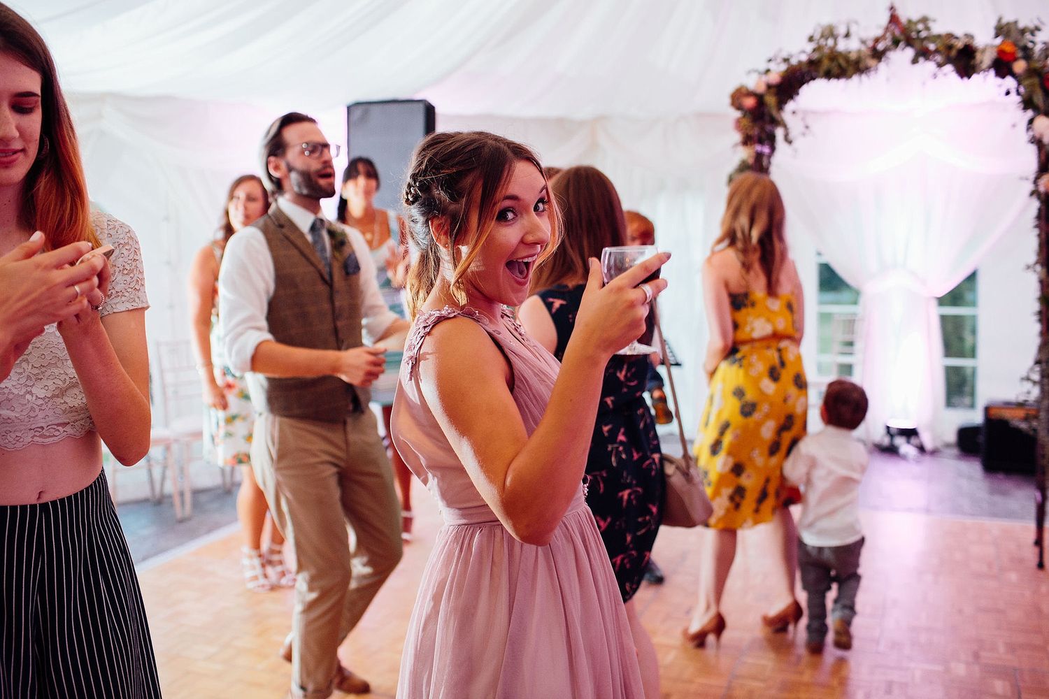 Wedding guests celebrate and dance inside an elegant white tent reception venue.