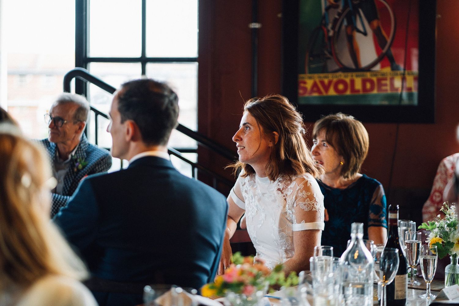 Wedding reception guests seated at elegant tables in a rustic indoor venue with large windows.