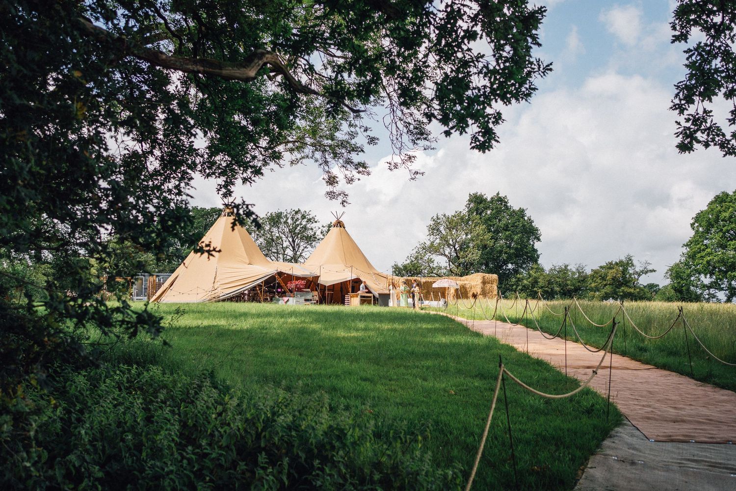 Panoramic view of a glamping site with multiple beige canvas bell tents set up on a lush green hillside.