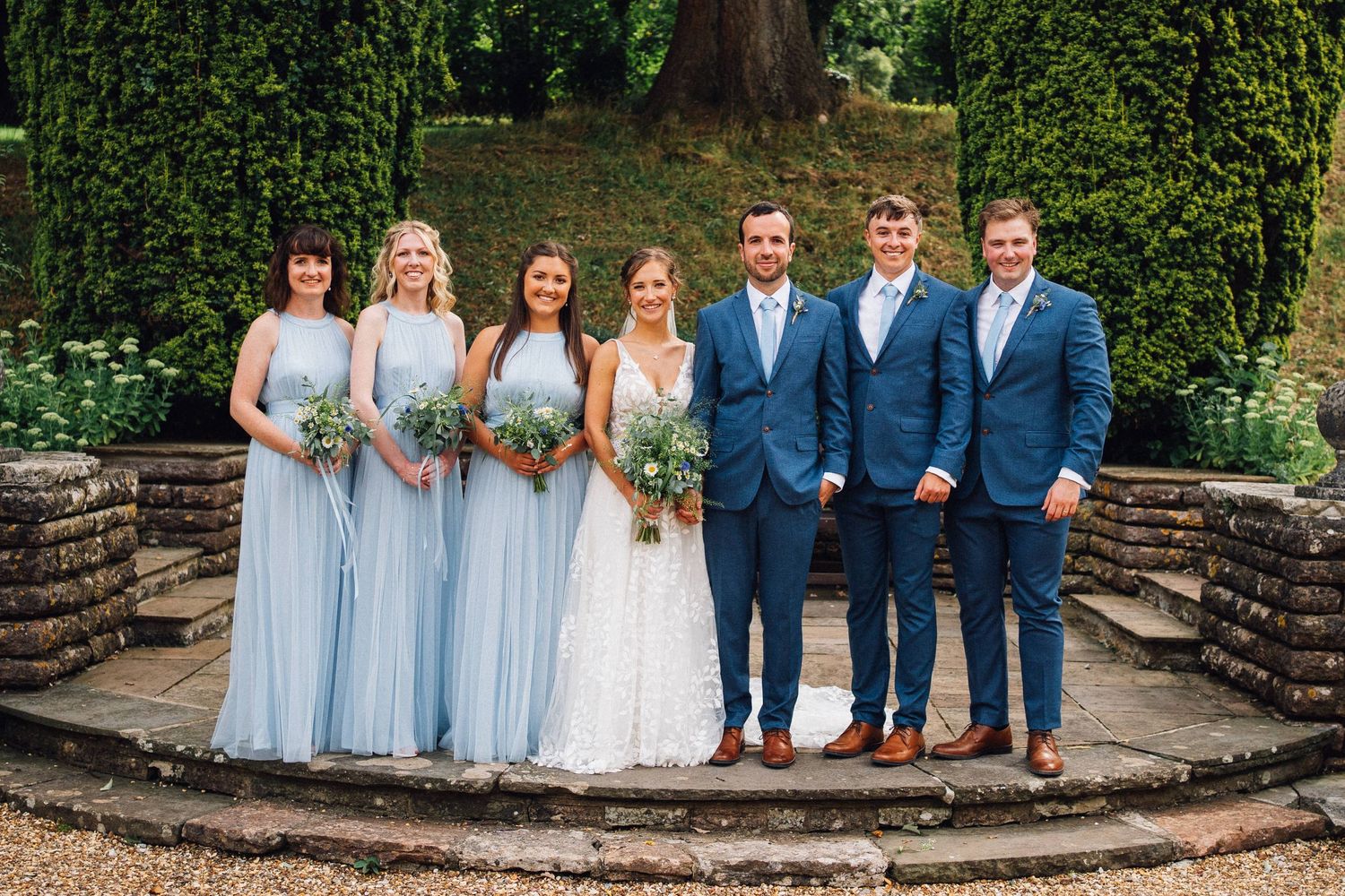 Wedding party lined up outdoors with bridesmaids in light blue dresses and groomsmen in navy suits.