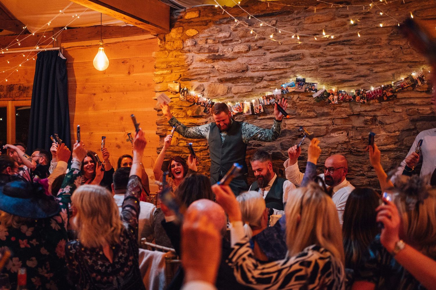 Wedding reception venue with warm lighting and exposed brick walls filled with celebrating guests.