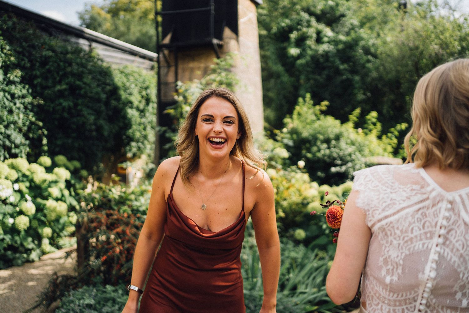 Two people share a joyful moment outdoors in a garden setting with lush greenery in the background.