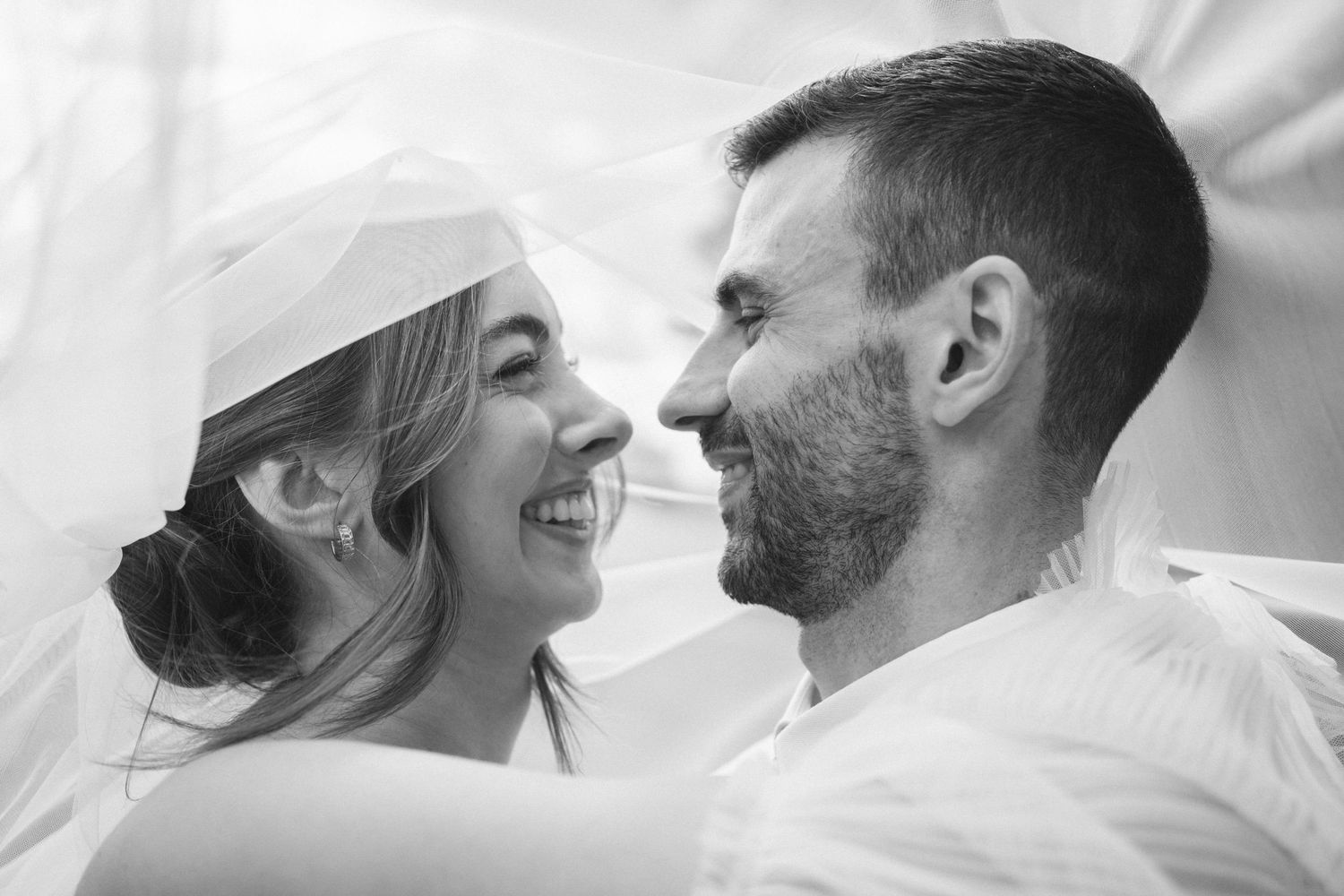 Black and white close up of a happy couple sharing an intimate moment under a veil.