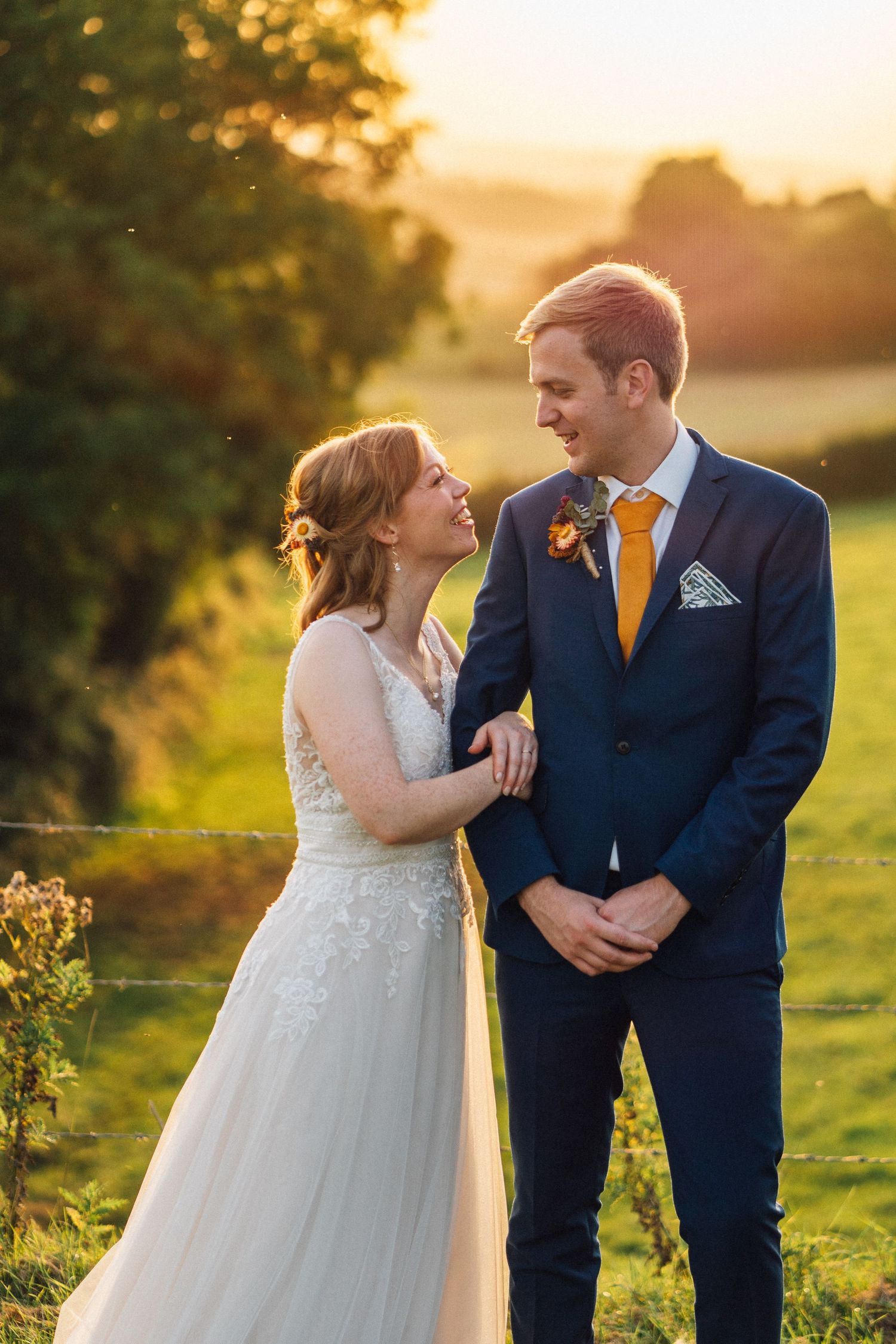 A couple shares joyful laughter together during their sunset wedding photoshoot in a golden-lit meadow.