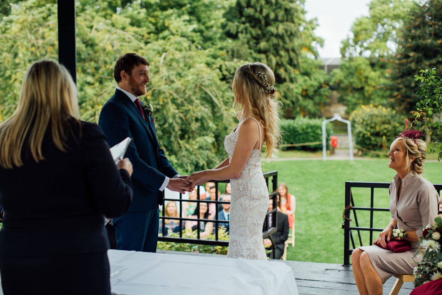 Bride and groom exchange vows outdoors at elegant garden wedding ceremony with guests seated nearby.