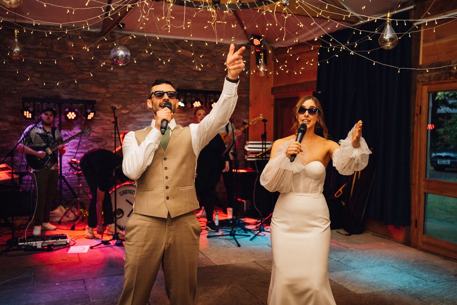 Performers singing and dancing during wedding reception with colorful lighting.