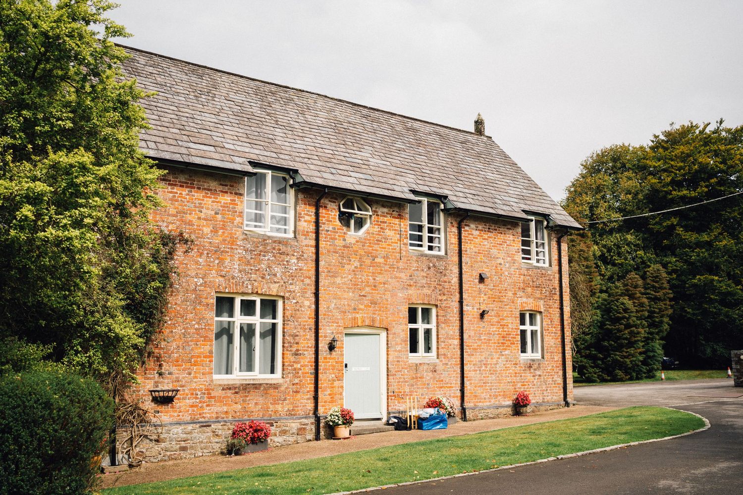Traditional brick country house with slate roof and symmetrical windows surrounded by greenery.