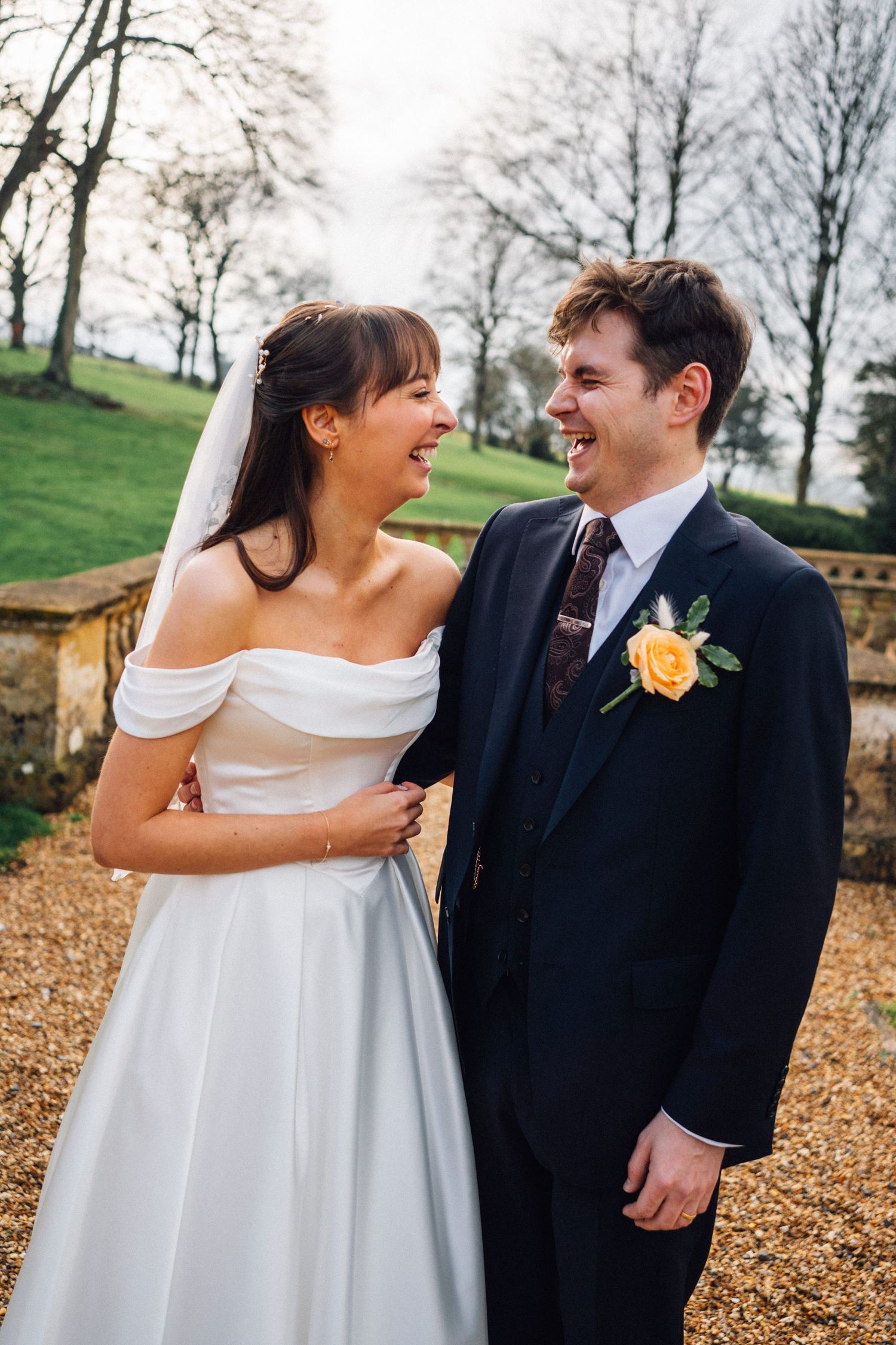 A joyful couple shares candid laughs during their autumn wedding photoshoot on fallen leaves.