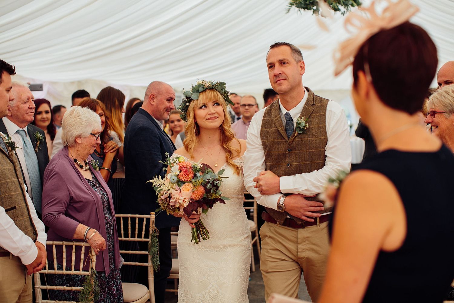 Wedding celebration in a white tent with guests mingling and floral arrangements.