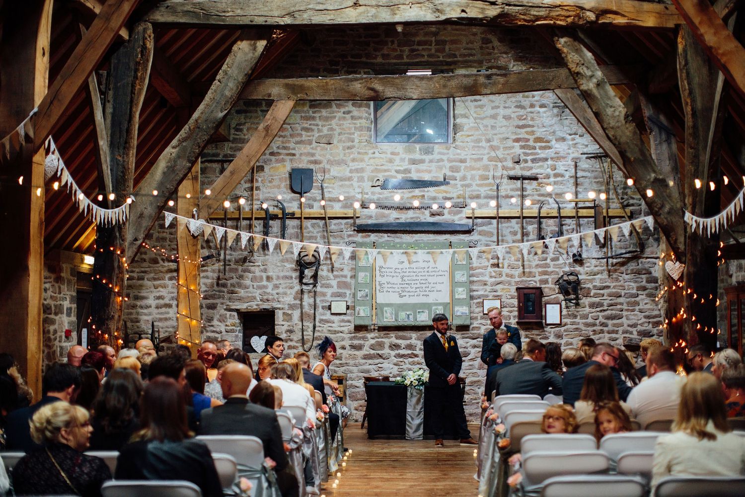 Wedding guests celebrate in a rustic barn venue decorated with string lights and bunting.
