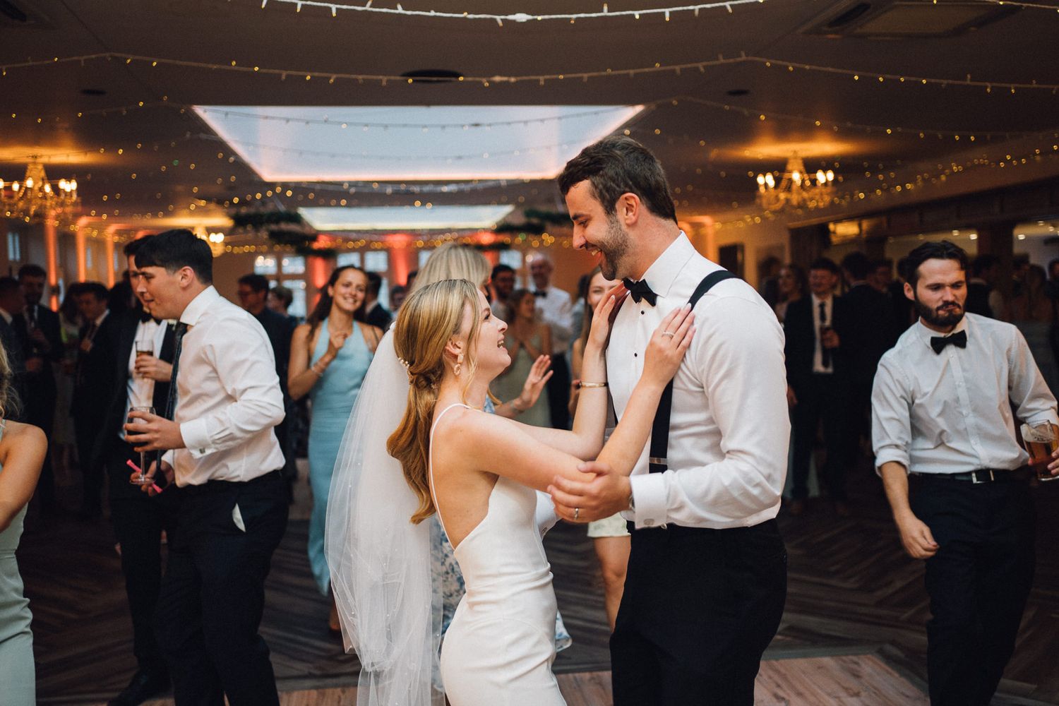 Wedding guests dance and celebrate on a warmly lit dance floor during an evening reception.