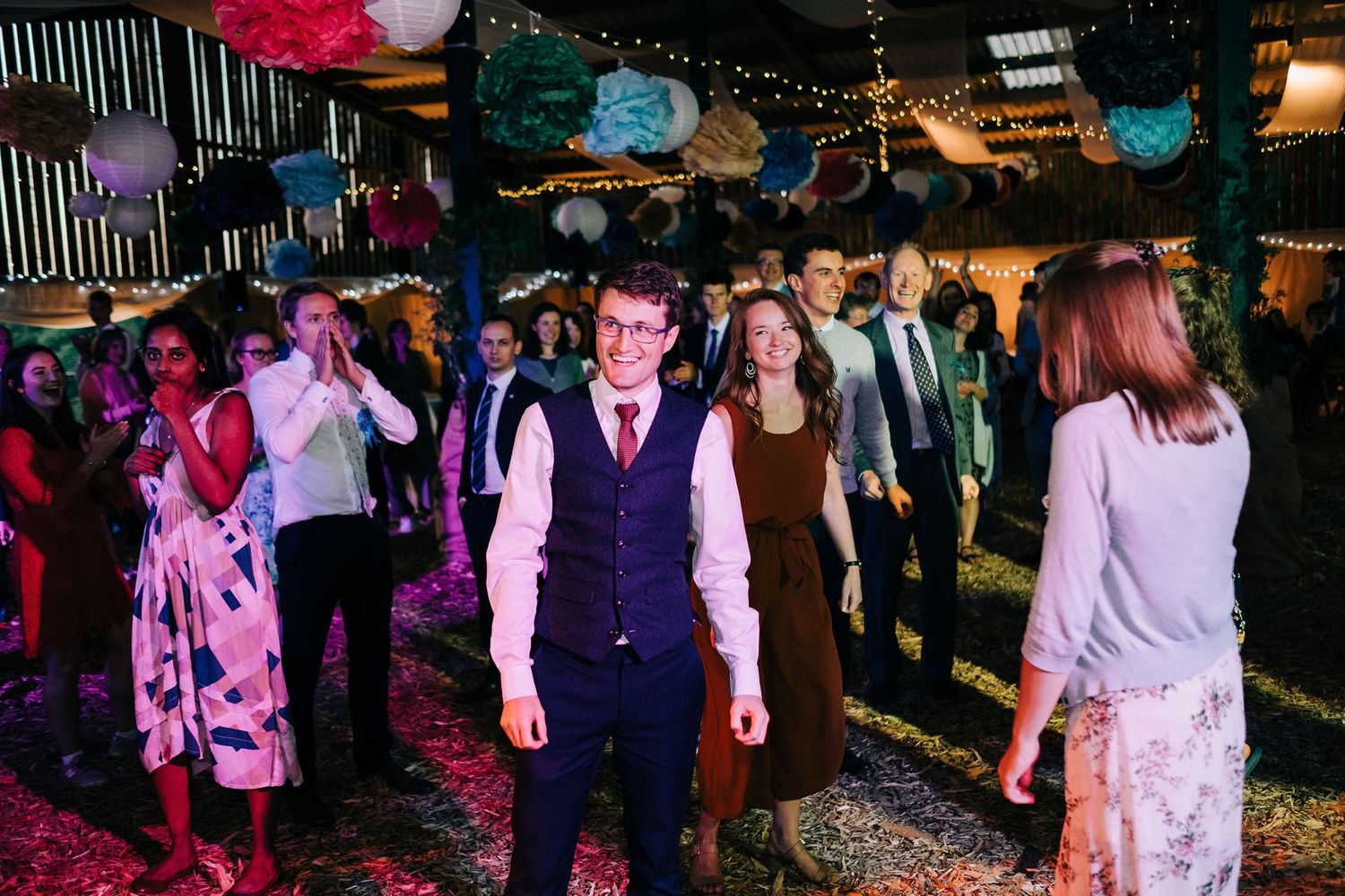 Wedding guests enjoying themselves on a dark dance floor illuminated by colorful party lights.