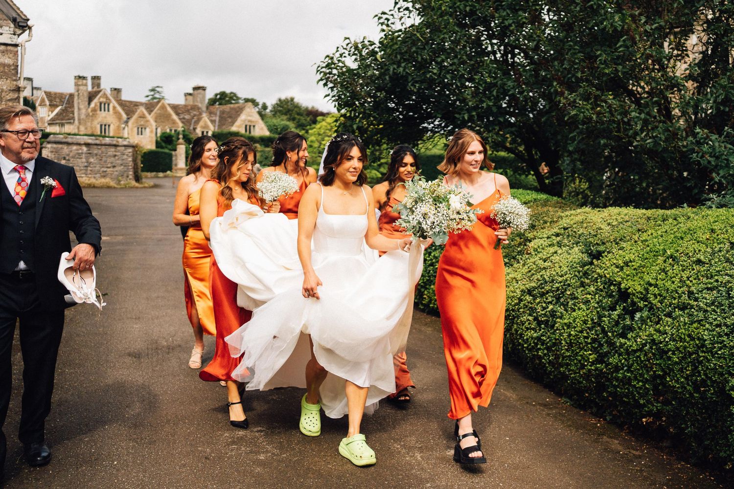 Wedding party in orange and white dresses walking along a garden path.