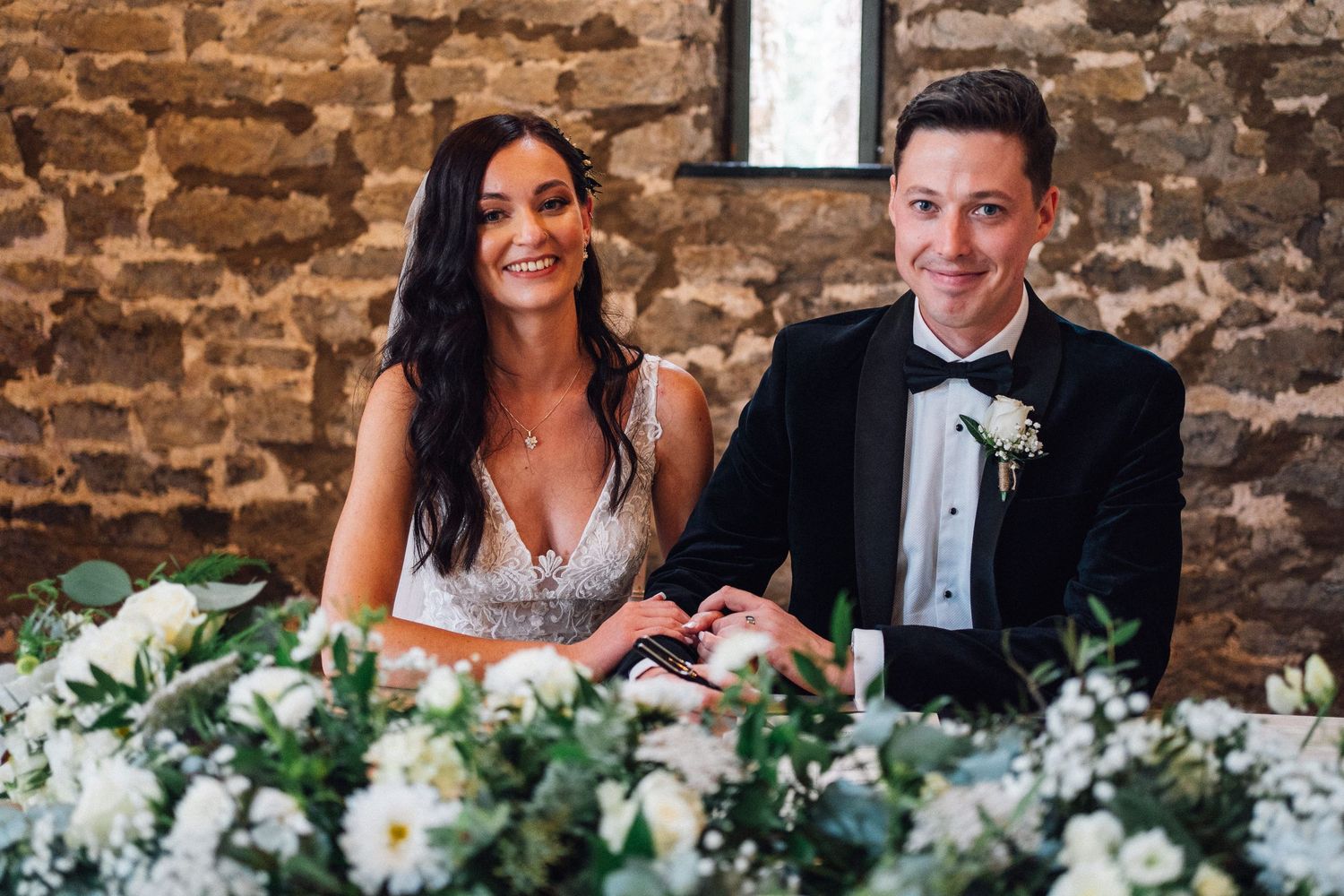 Wedding celebration in historic stone barn with white floral arrangements on tables.