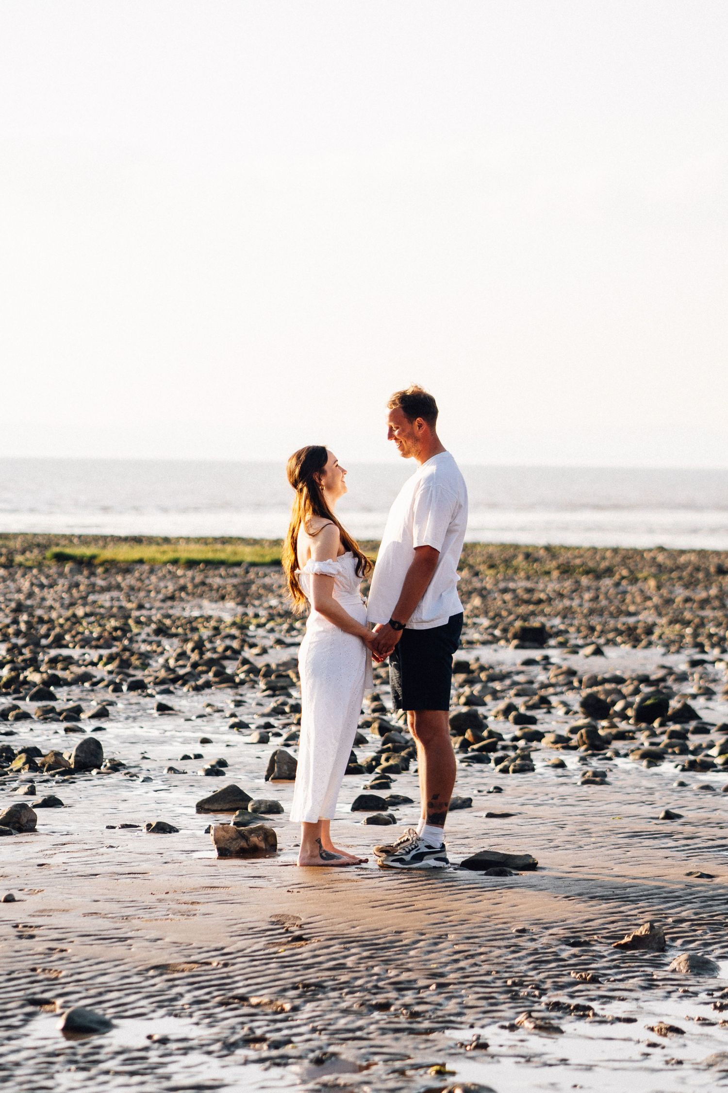 Couple standing among rocky beach terrain during golden hour photography session.
