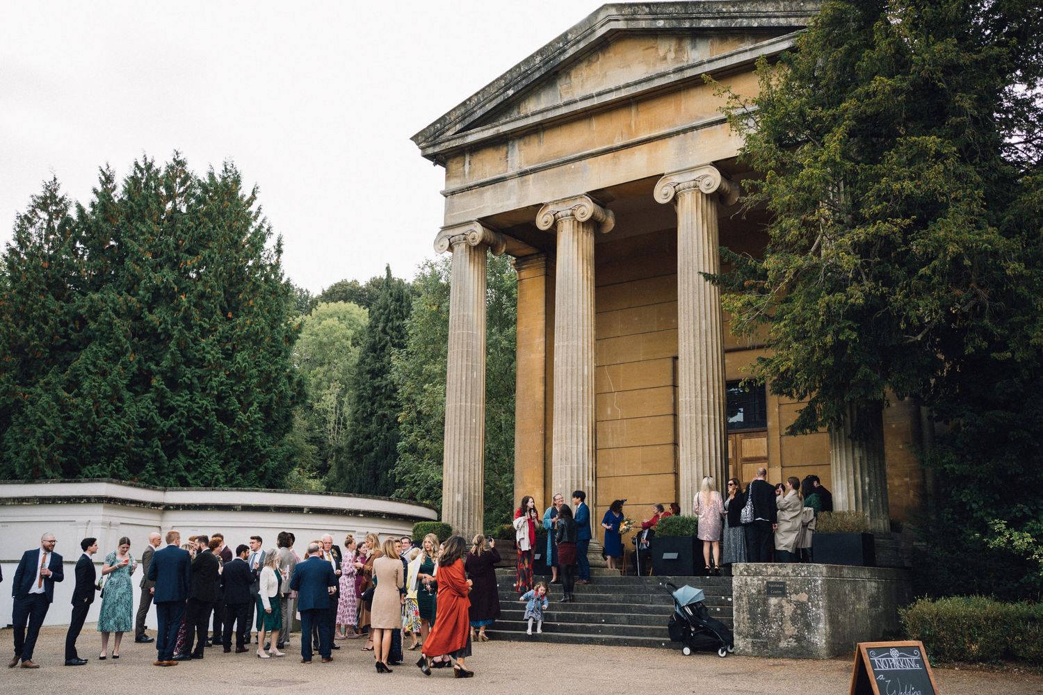 Wedding guests gather outside a grand classical building with columns during an outdoor ceremony.