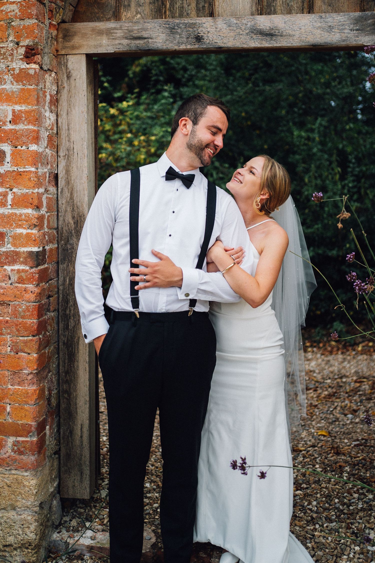 Romantic wedding couple shares intimate moment against rustic brick and wood backdrop.
