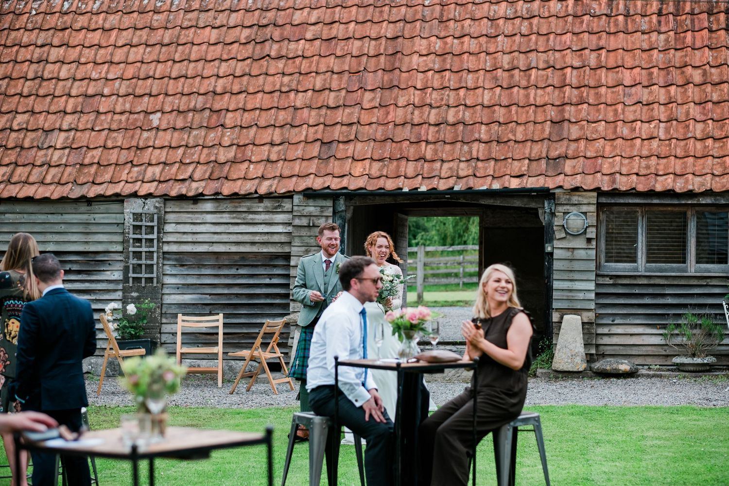 Outdoor wedding reception setup with green chairs and tables against a rustic barn backdrop.
