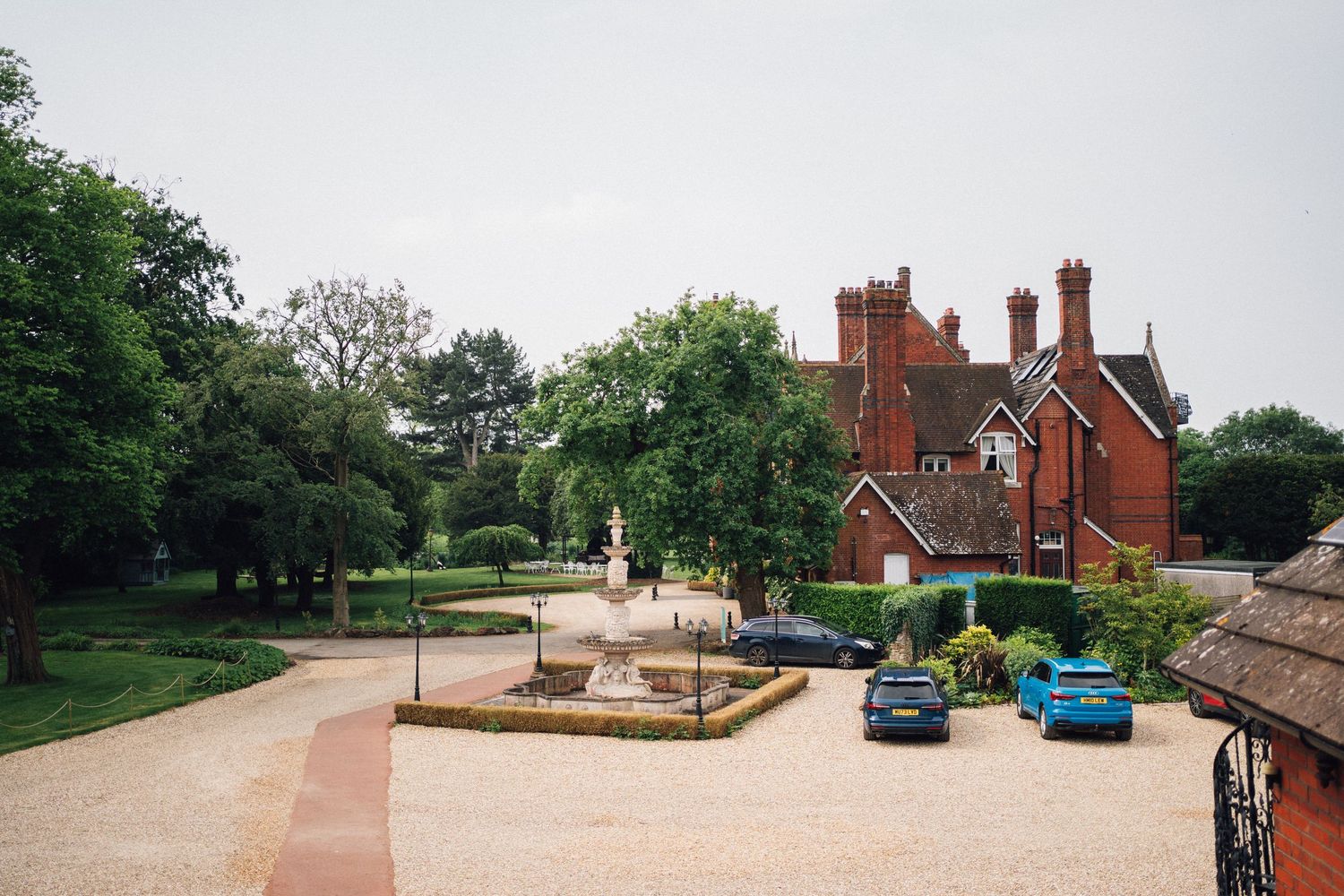A panoramic view of a red brick mansion and its surrounding grounds with paved walkways and landscaped gardens.