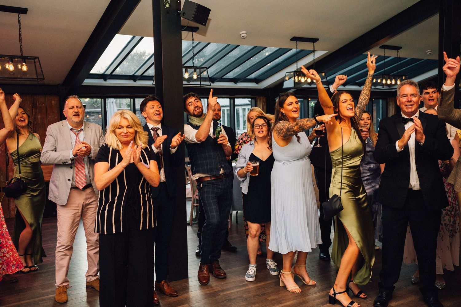 Wedding guests dance and celebrate on a dimly lit dance floor during a reception party.